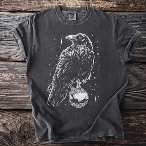 T-shirt with white line art of a crow holding a decorative orb amidst stars.