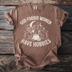 Brown t-shirt with white graphic of three cats, cauldron, and moon, reading "God forbid women have hobbies".