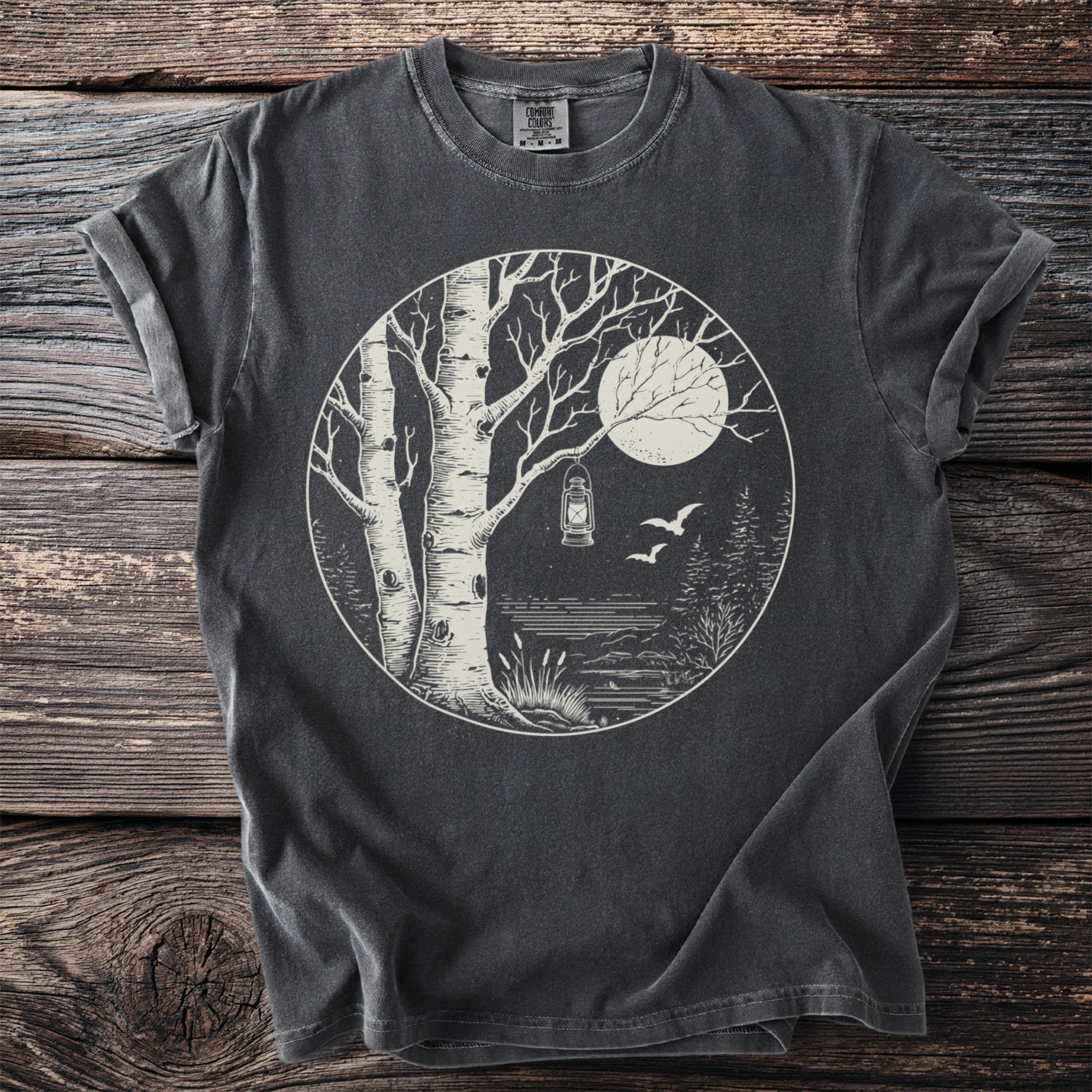 Dark t-shirt with a circular graphic of a moonlit forest scene with birches and a lantern.