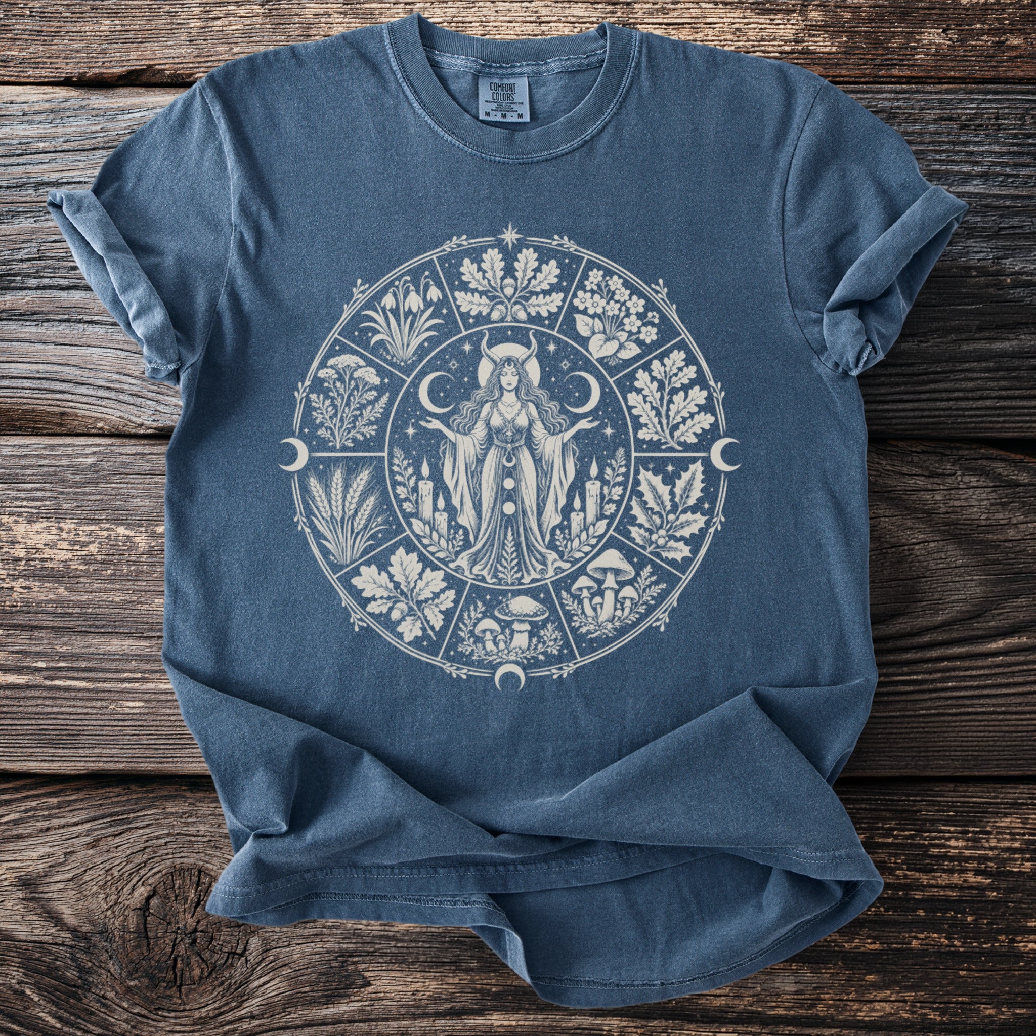 Blue t-shirt with a circular pagan-themed graphic featuring a woman, plants, and celestial symbols.