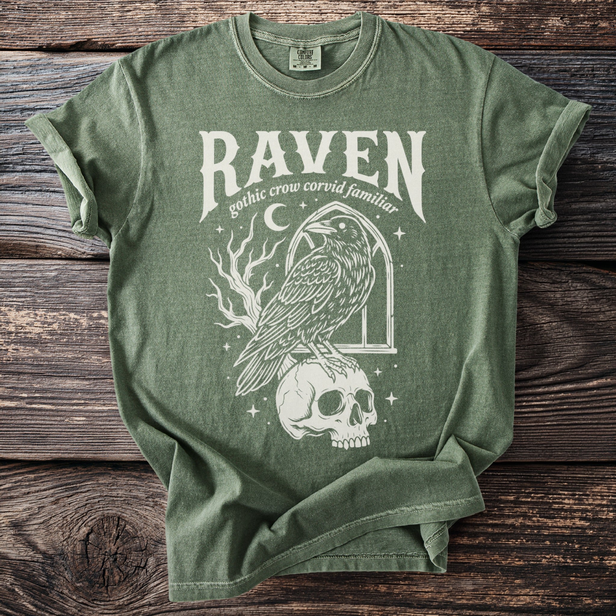 Green t-shirt with a raven perched on a skull, text reads "Raven gothic crow corvid familiar".