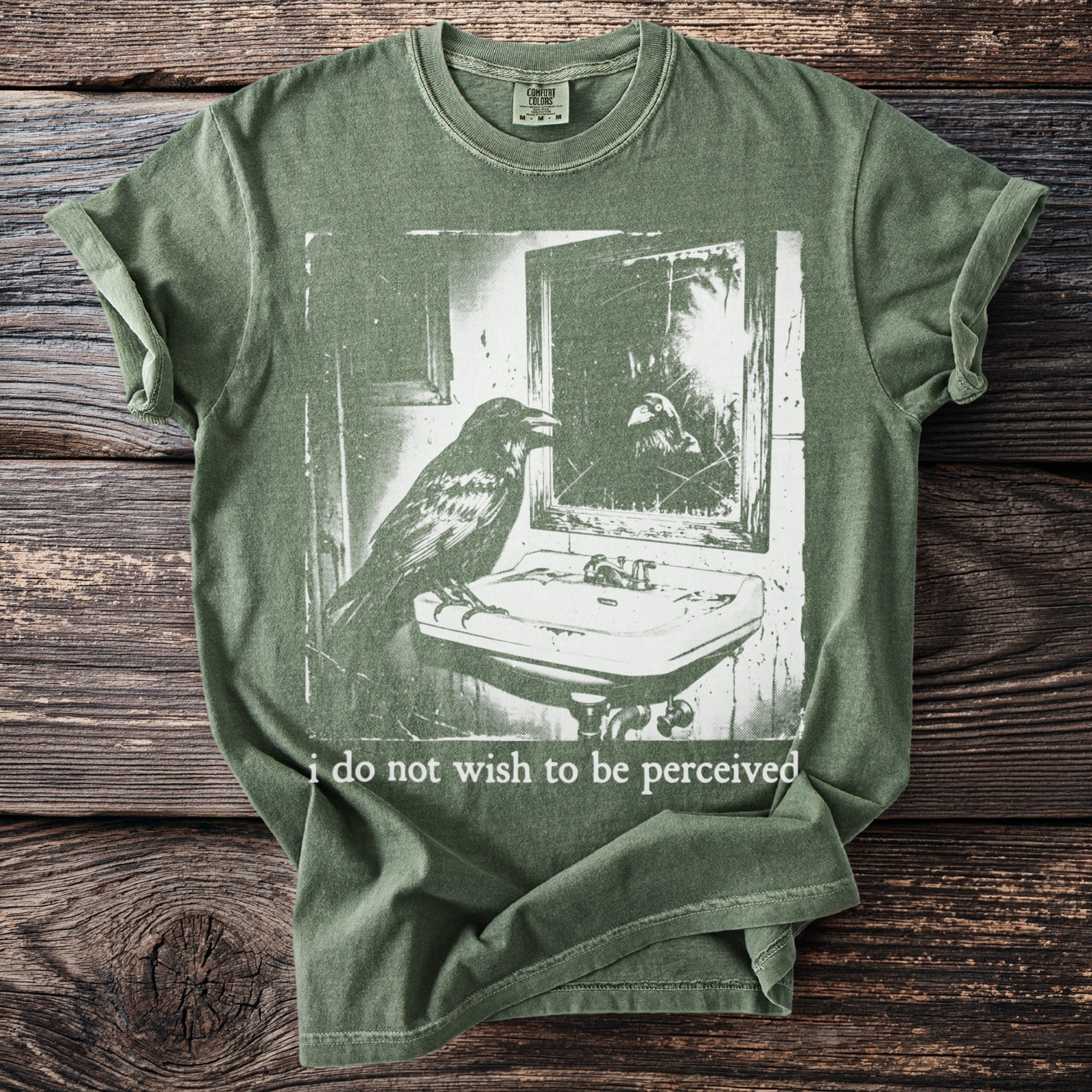 Green t-shirt with a raven at a sink and the text "i do not wish to be perceived".
