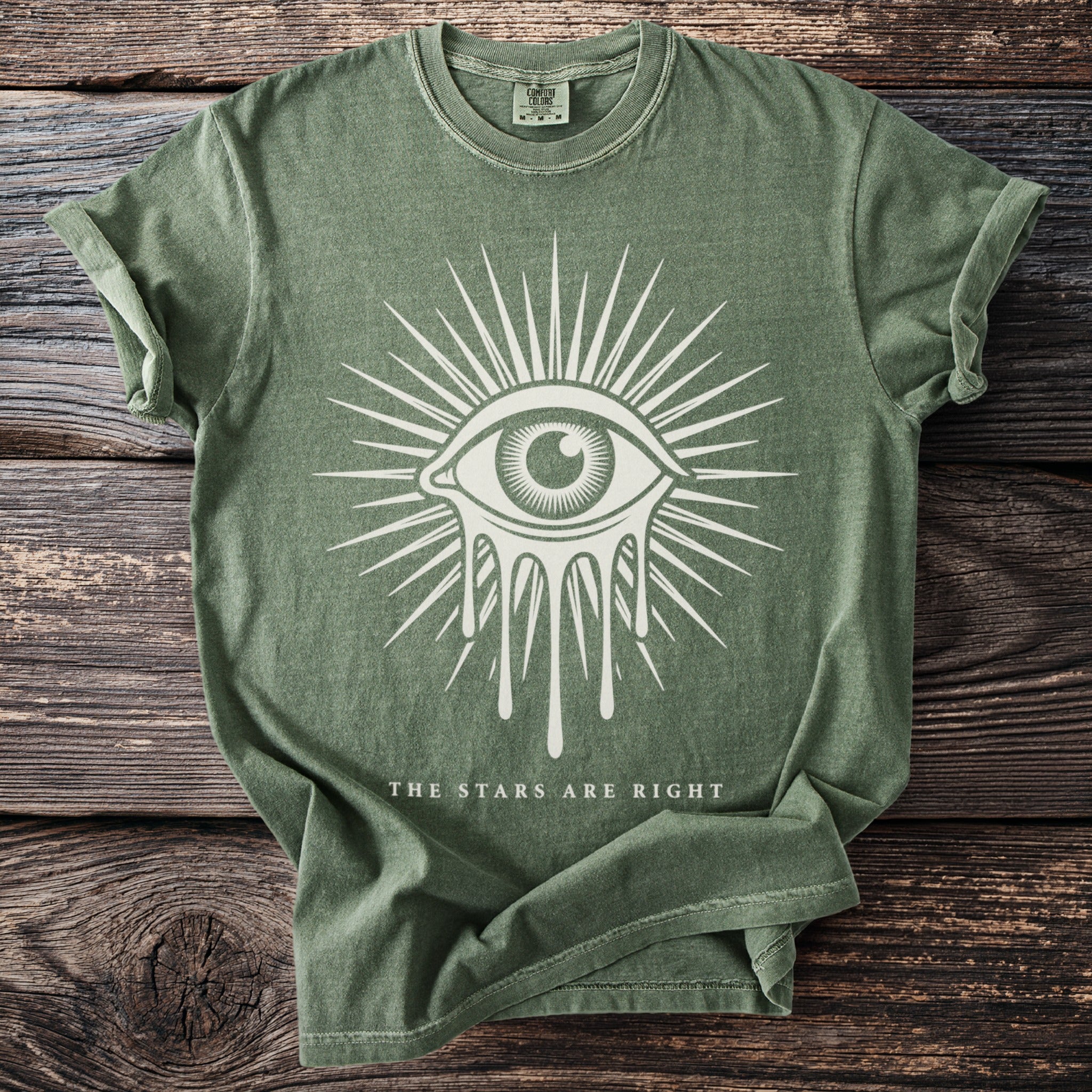 Green t-shirt with a dripping eye and radiating lines graphic, and text "THE STARS ARE RIGHT".