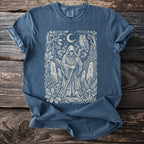 Blue t-shirt with a white, mystical forest scene featuring a hooded figure and owl.