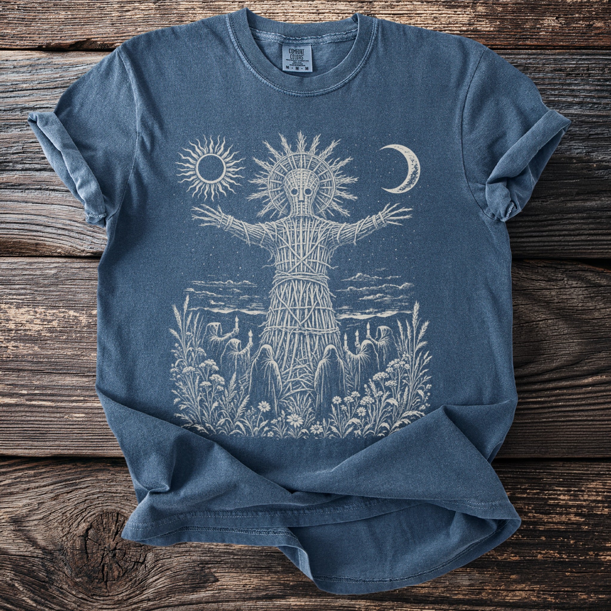 Blue t-shirt with cream print of a wicker man figure, sun, moon, and hooded figures.