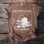 Brown t-shirt with "god forbid women have hobbies" text and vintage illustration.