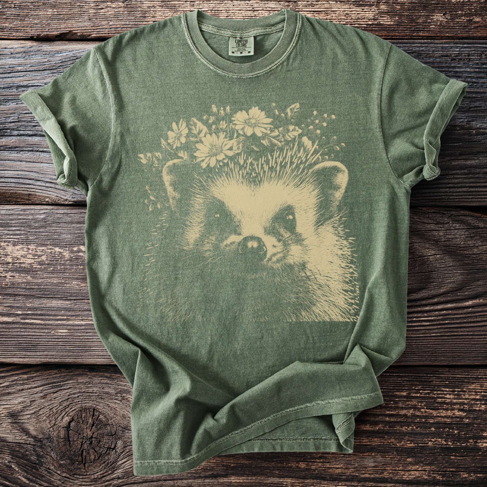 Green t-shirt with a cream-colored graphic of a hedgehog wearing a flower crown.