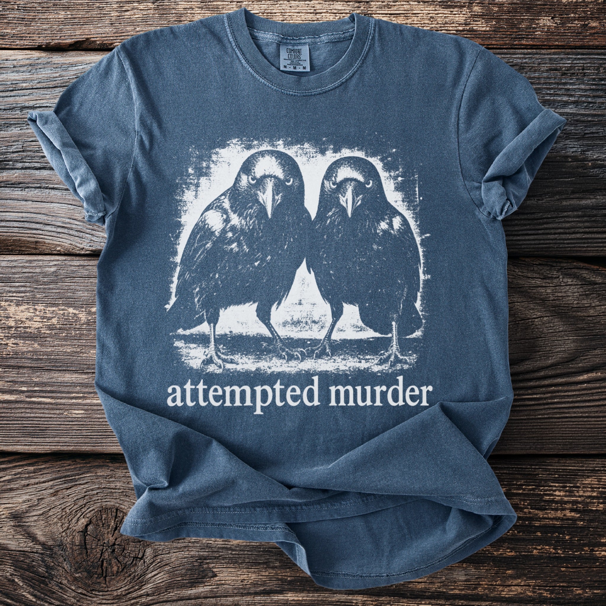 Blue t-shirt with white graphic of two crows and the text "attempted murder."
