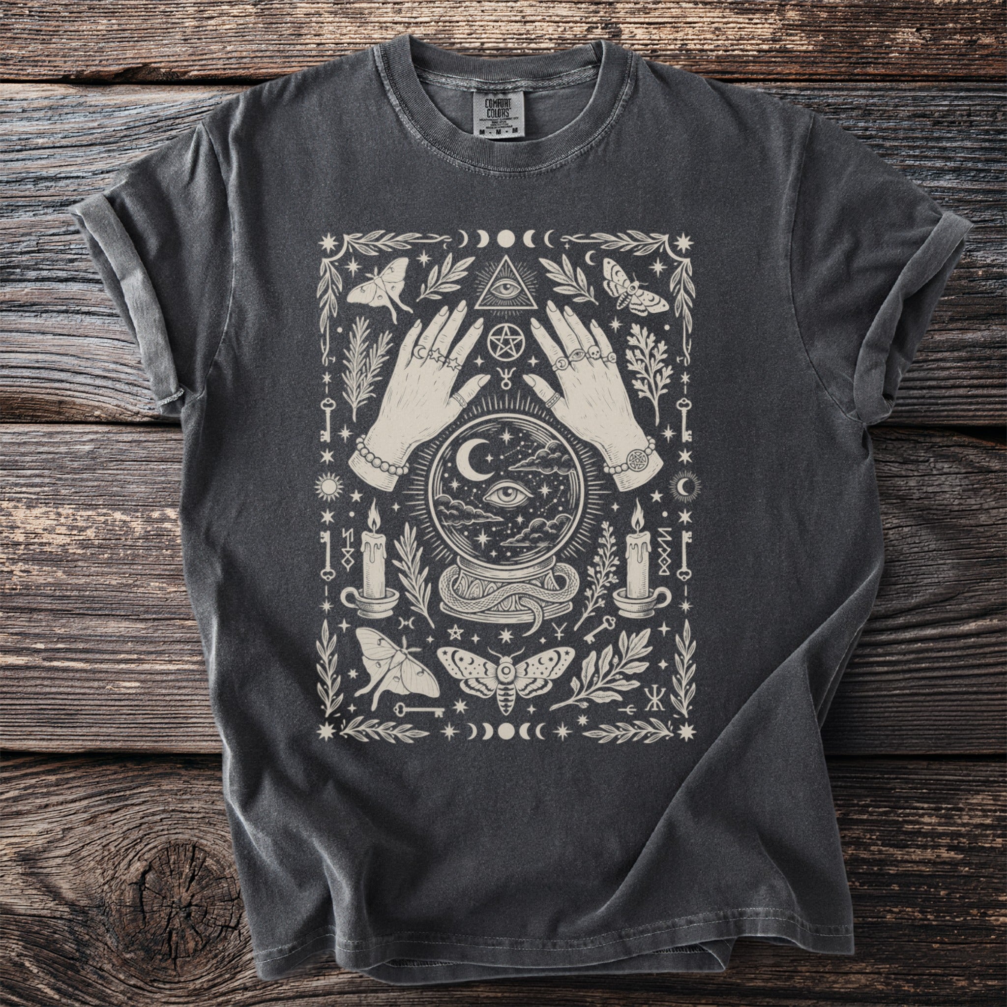 Dark grey t-shirt with a mystical celestial design featuring hands, crystal ball, moths, candles, and keys.
