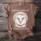 Brown Comfort Colors t-shirt with a barn owl graphic and text "patron saint of running on no sleep."