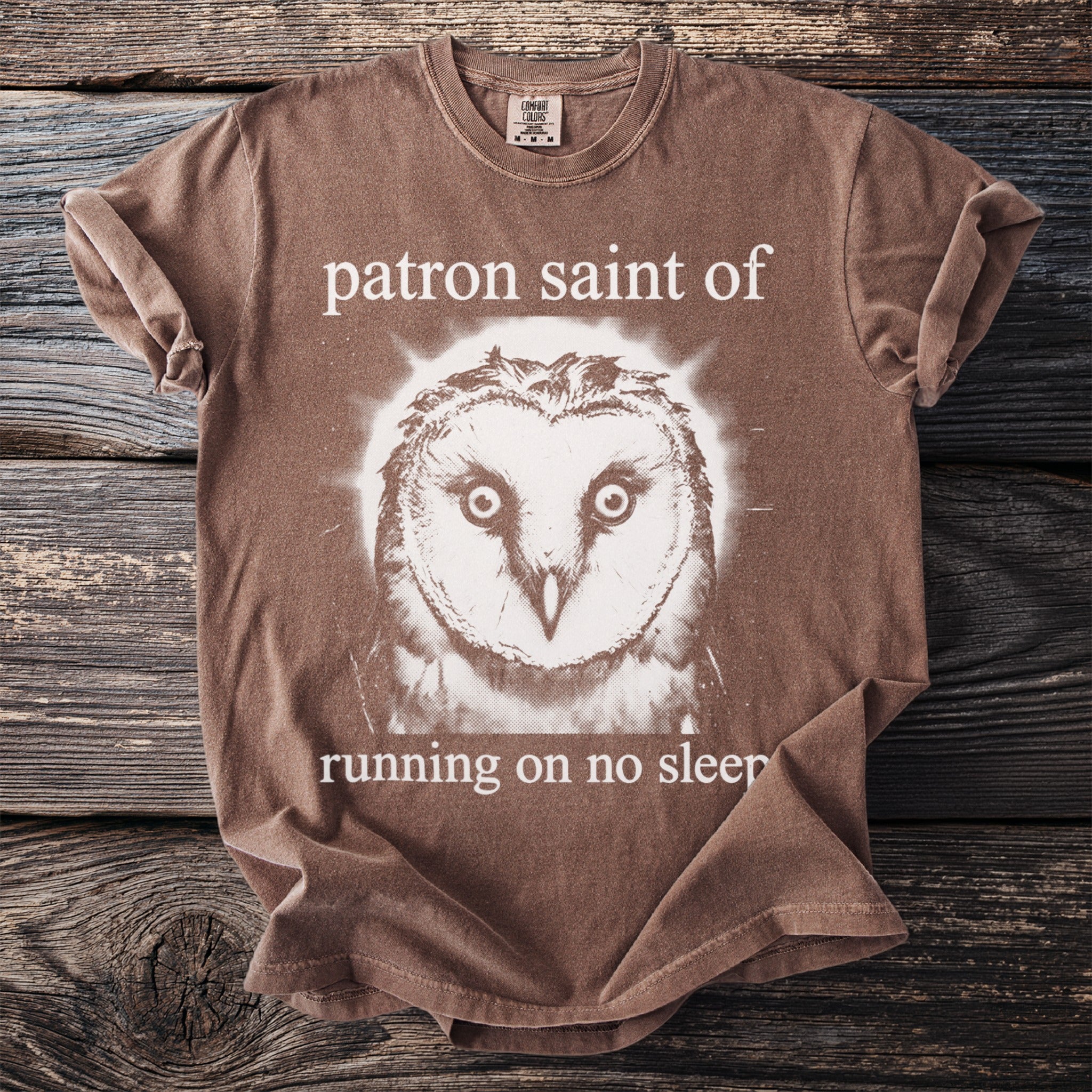 Brown Comfort Colors t-shirt with a barn owl graphic and text "patron saint of running on no sleep."