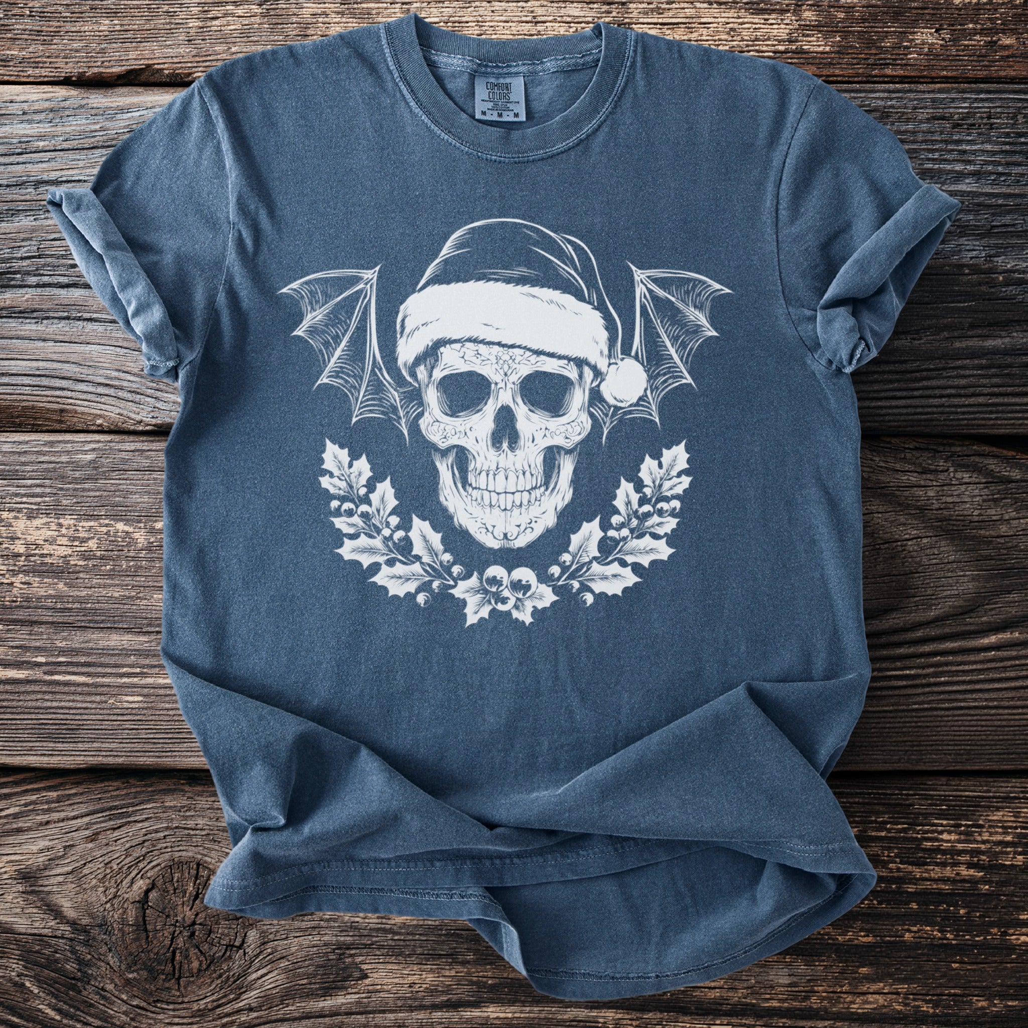 Blue t-shirt with white Christmas skull, bat wings, and holly wreath graphic.