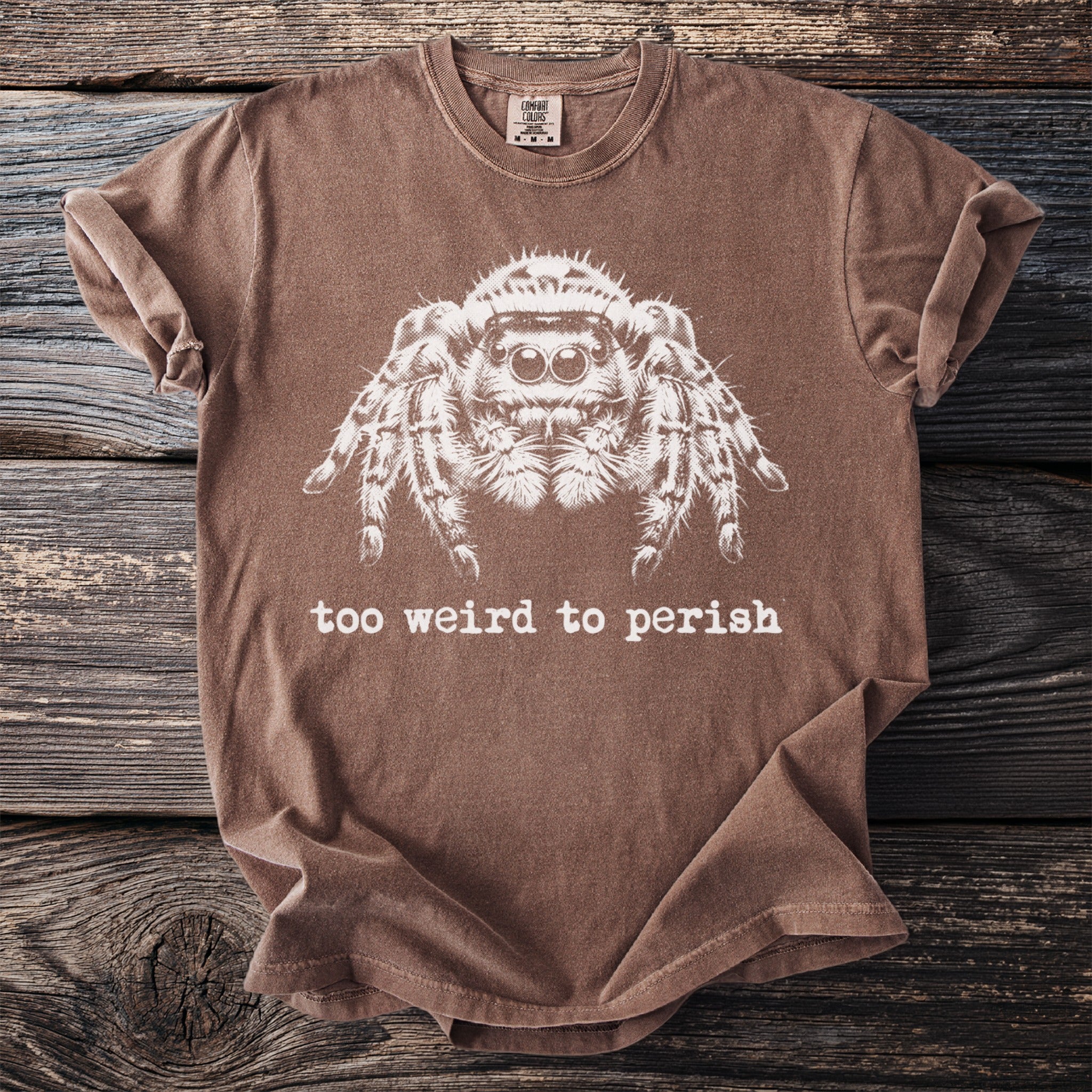 Brown t-shirt with white jumping spider graphic and text "too weird to perish".