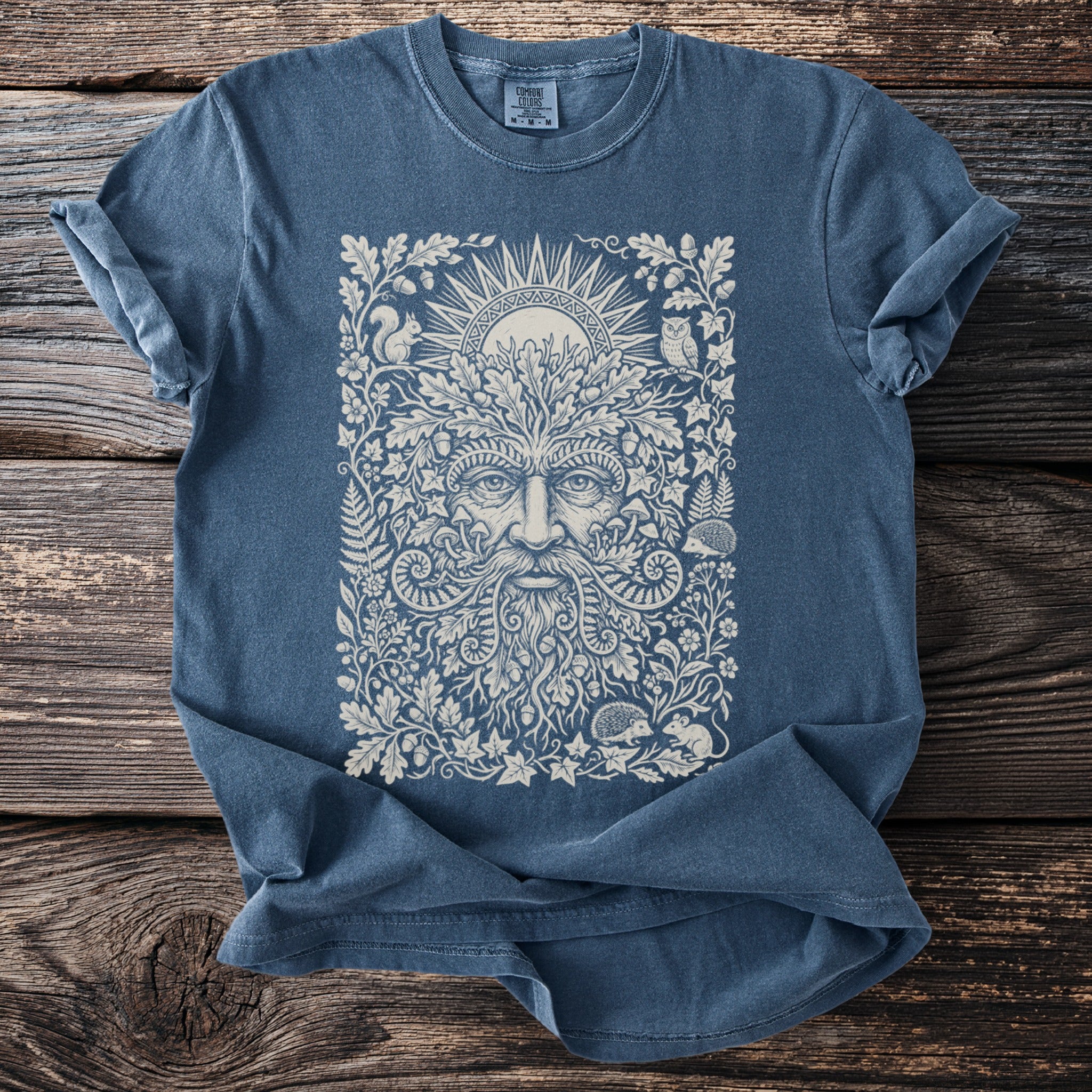 Blue t-shirt with a nature-themed print of a green man, sun, owl, squirrel, and hedgehogs.