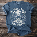 Blue t-shirt with vintage graphic of witches dancing around a bonfire, text reads "God forbid women have hobbies".