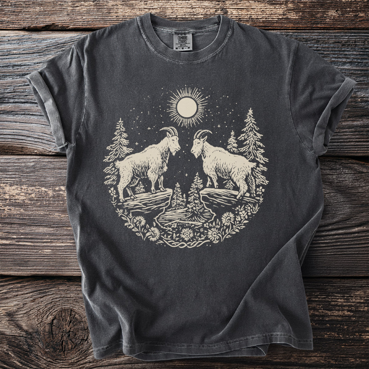 Dark t-shirt with cream graphic of two mountain goats, trees, moon, and flowers.
