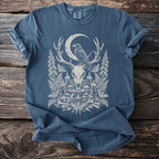 Blue t-shirt with cream graphic of a raven on deer antlers, skull, moon, and ornate nature elements.