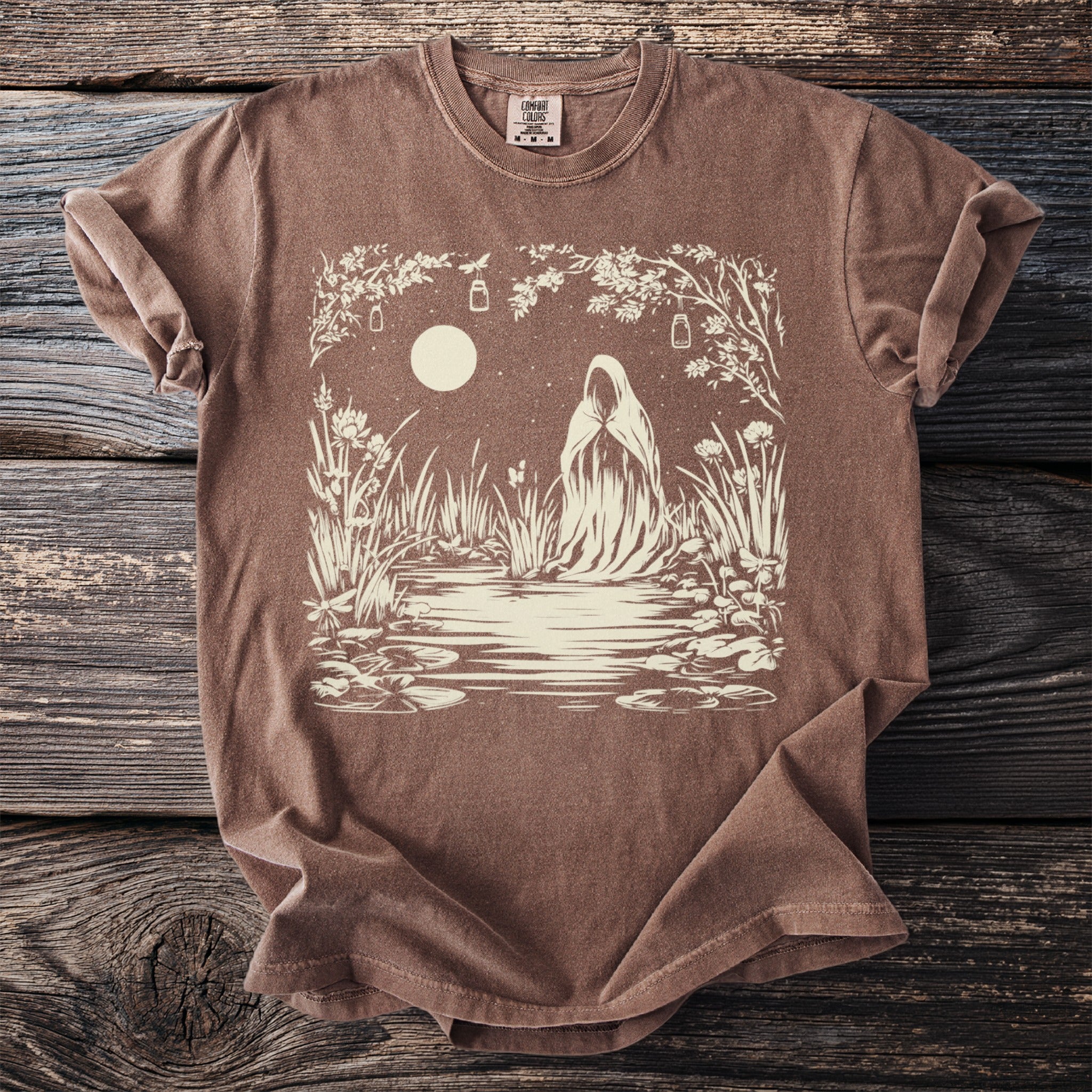 Brown t-shirt with a cream-colored graphic of a cloaked figure at a moonlit pond.