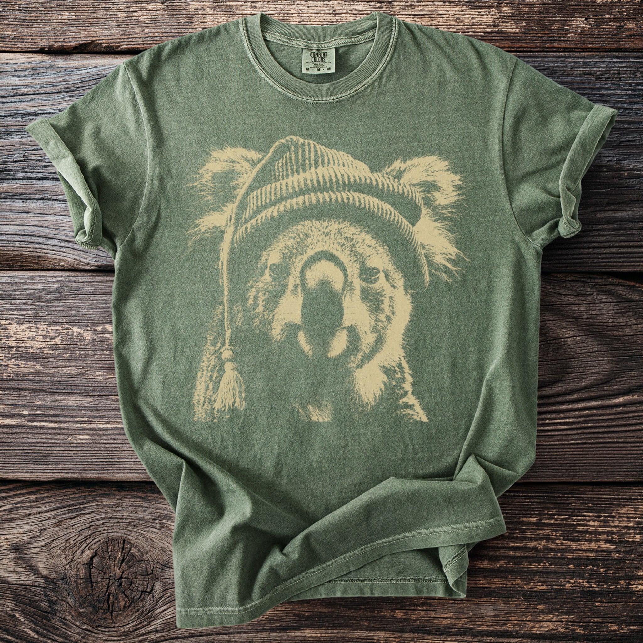 Green t-shirt with a beige distressed print of a koala wearing a beanie.