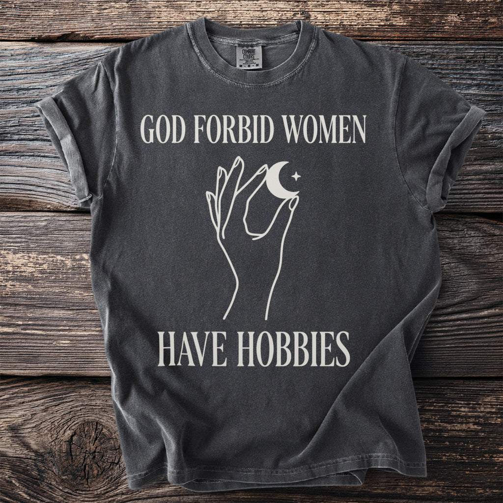 Dark grey t-shirt with text "GOD FORBID WOMEN HAVE HOBBIES" and celestial graphic.