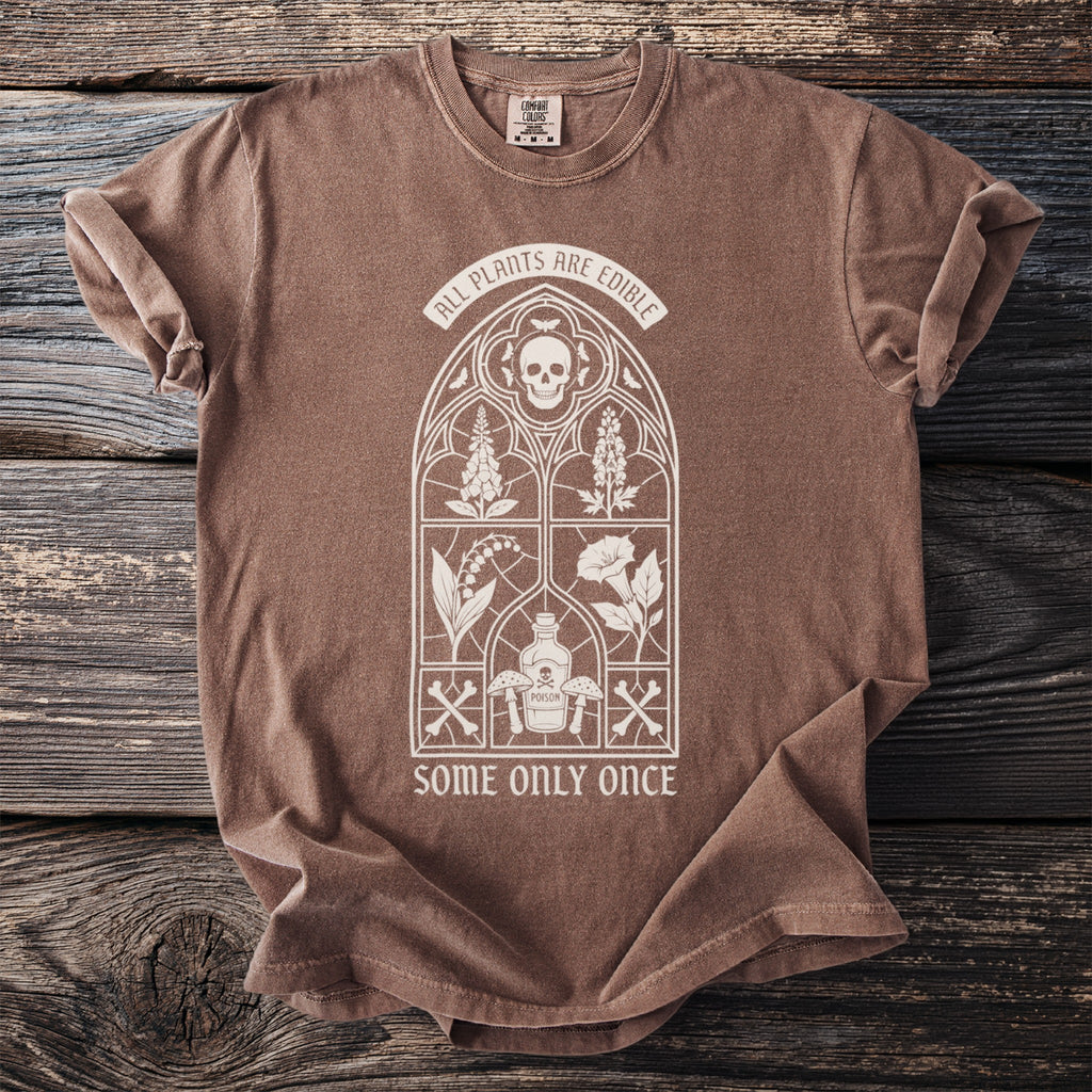 Brown t-shirt with a white graphic of a stained glass window featuring skulls, plants, mushrooms, and text.