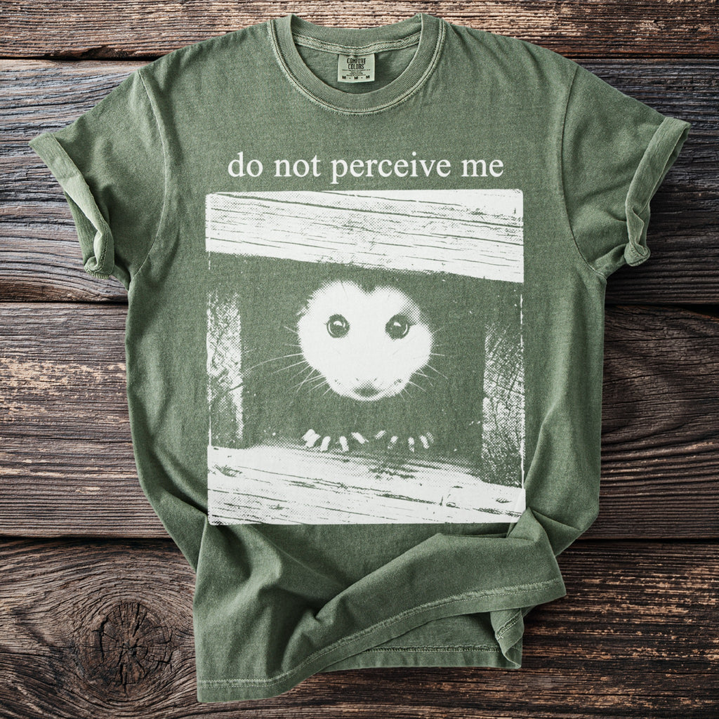 Green t-shirt with a white graphic of an opossum's face and text "do not perceive me".