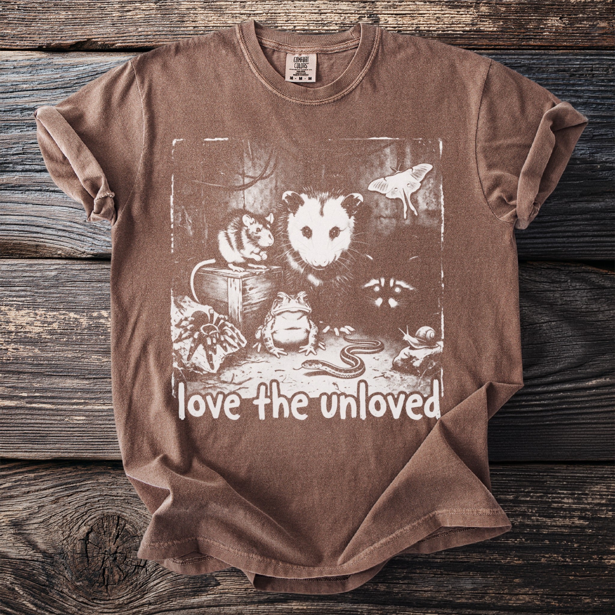 Brown t-shirt with illustration of possum, rat, frog, spider, snake, snail, moth, and text "love the unloved".