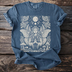 Blue t-shirt with a white moth woman, moon, stars, roses, ferns, and mushrooms design.