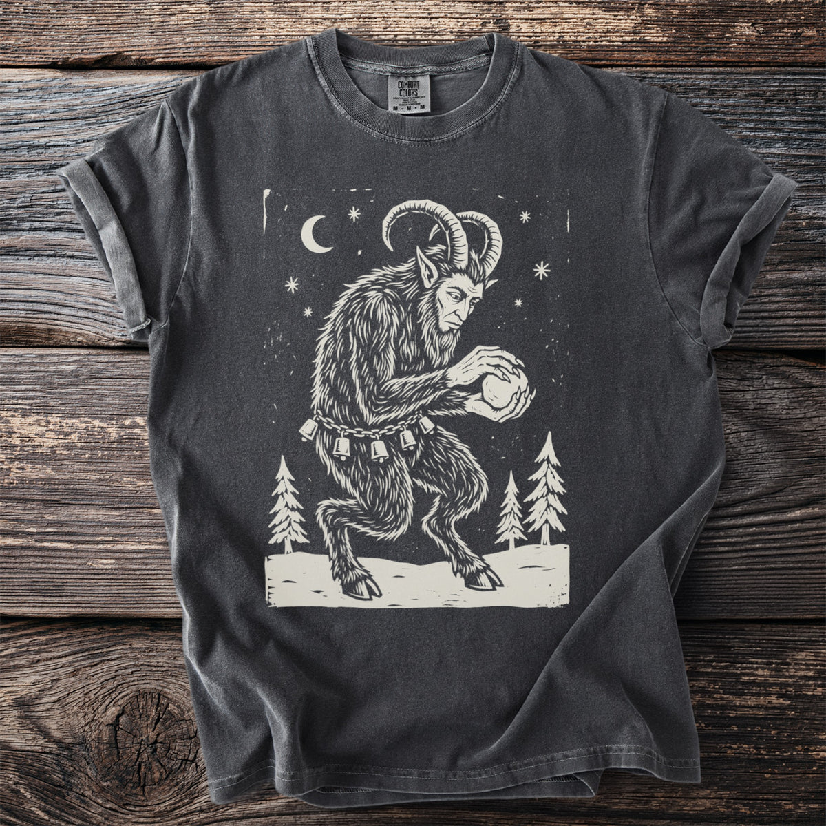 Pepper gray t-shirt with a cream folk-cut print: Krampus crouches among snowy pines, packing a snowball between his clawed hands.