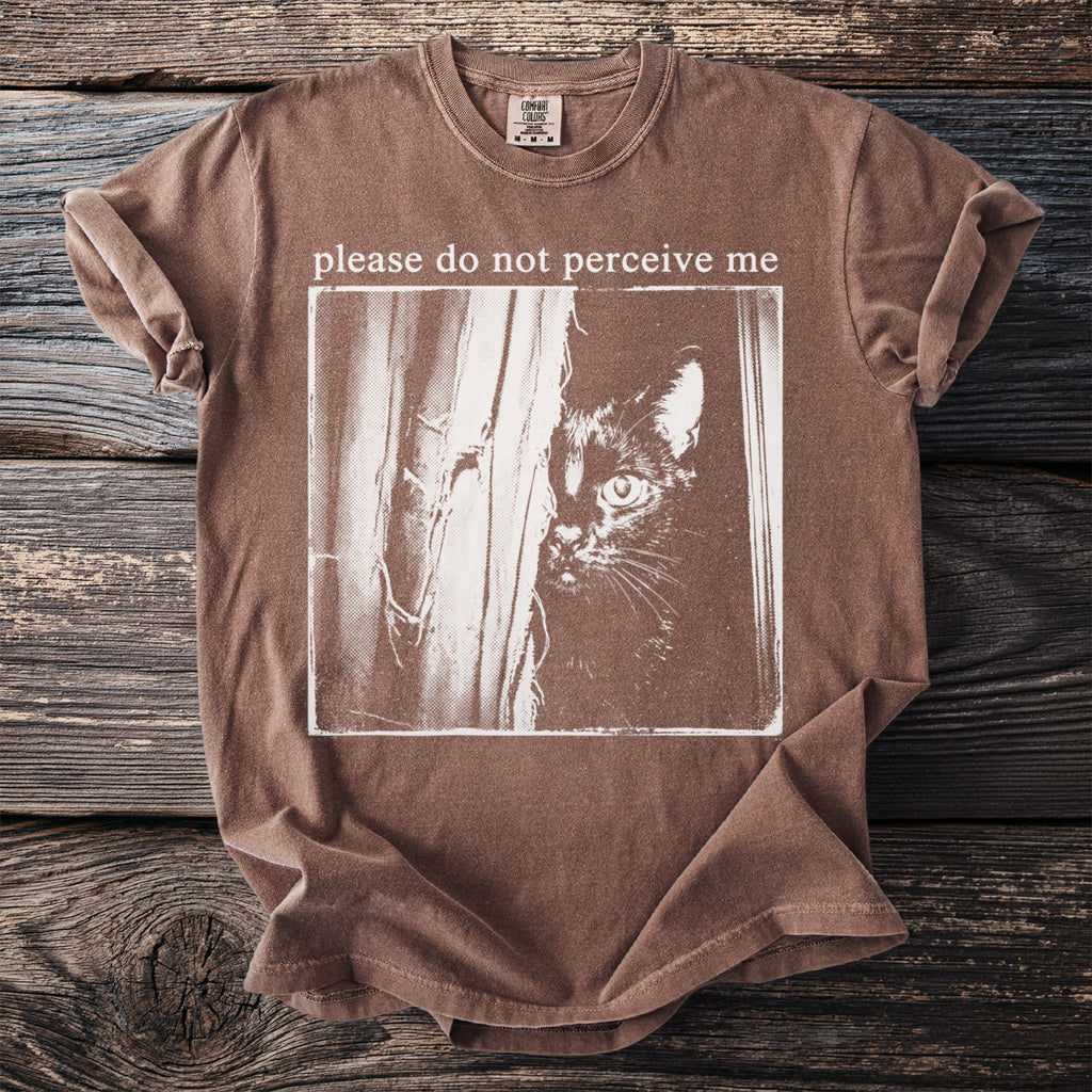 Brown t-shirt with a black cat peeking from behind curtains, text "please do not perceive me" above.