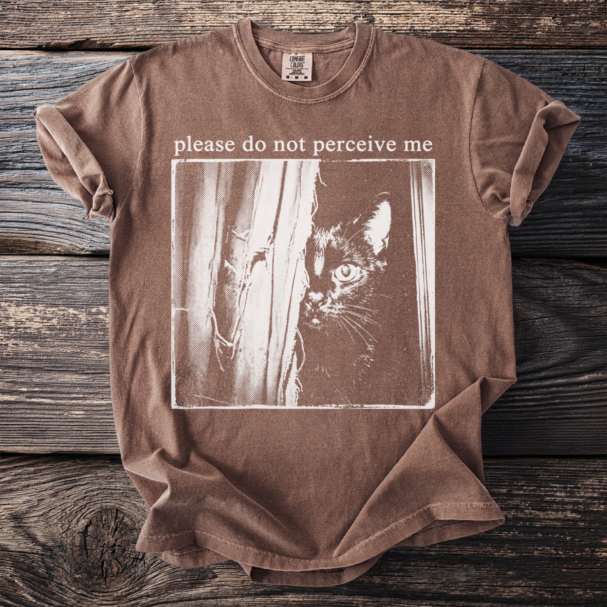 Brown t-shirt with a black cat peeking from behind curtains, text "please do not perceive me" above.
