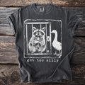T-shirt with a graphic of a raccoon in a cage holding a spoon and a goose next to it with text "got too silly."