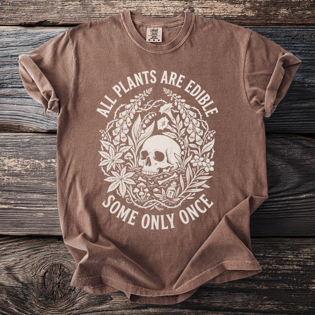 Brown t-shirt with a white circular graphic of a skull surrounded by plants and the text "ALL PLANTS ARE EDIBLE SOME ONLY ONCE".