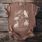 Brown t-shirt with 'The Witch's Familiars' illustration of a cat, owl, raven, bat, toad, and hare.