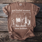 Brown t-shirt with "god forbid women have hobbies" text and witch illustration.