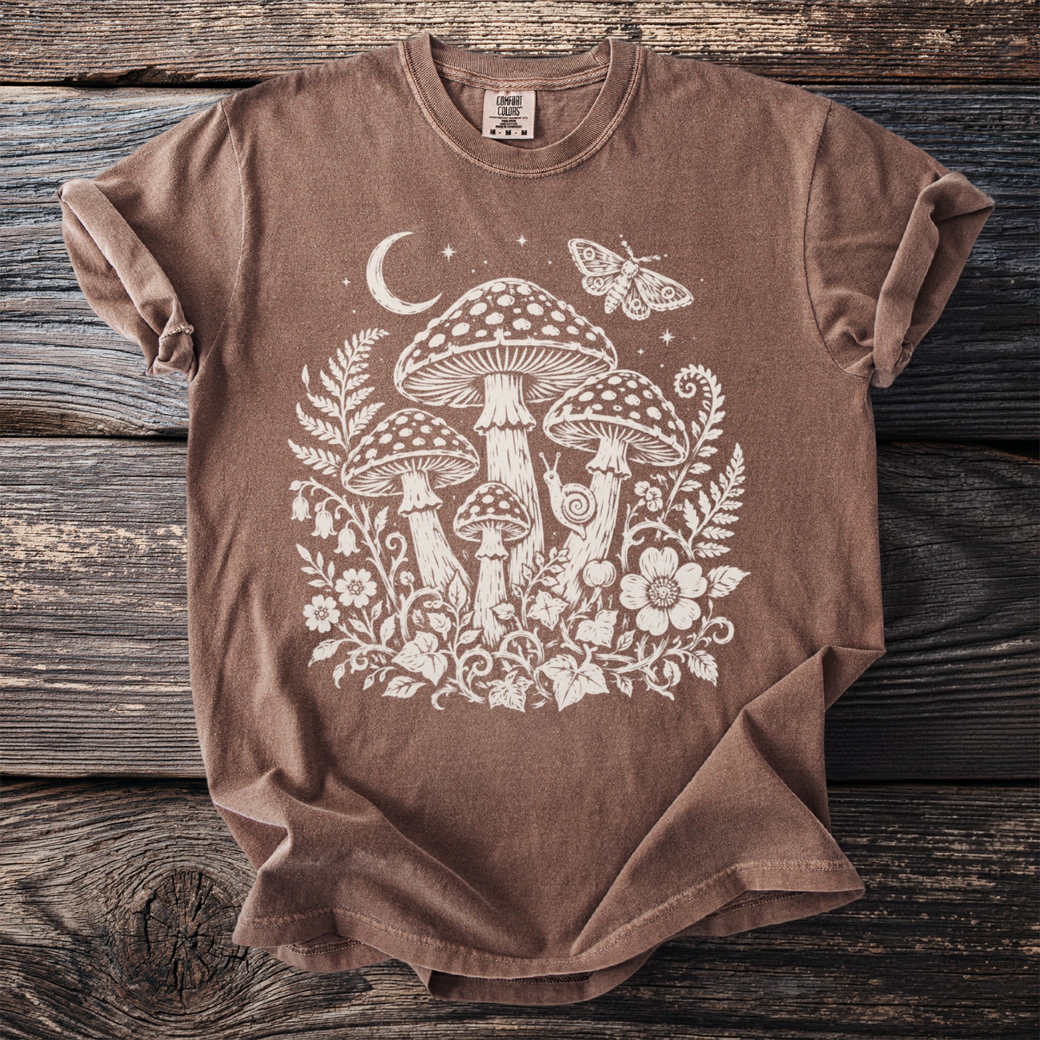 Brown t-shirt with white cream-colored mushroom, moth, and floral graphic.