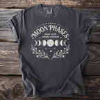 Dark t-shirt featuring white "Moon Phases" text, lunar cycle graphic, and floral wreathes.