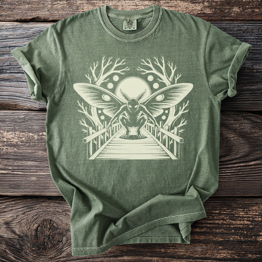 Olive green t-shirt with moth-like creature on a bridge graphic.