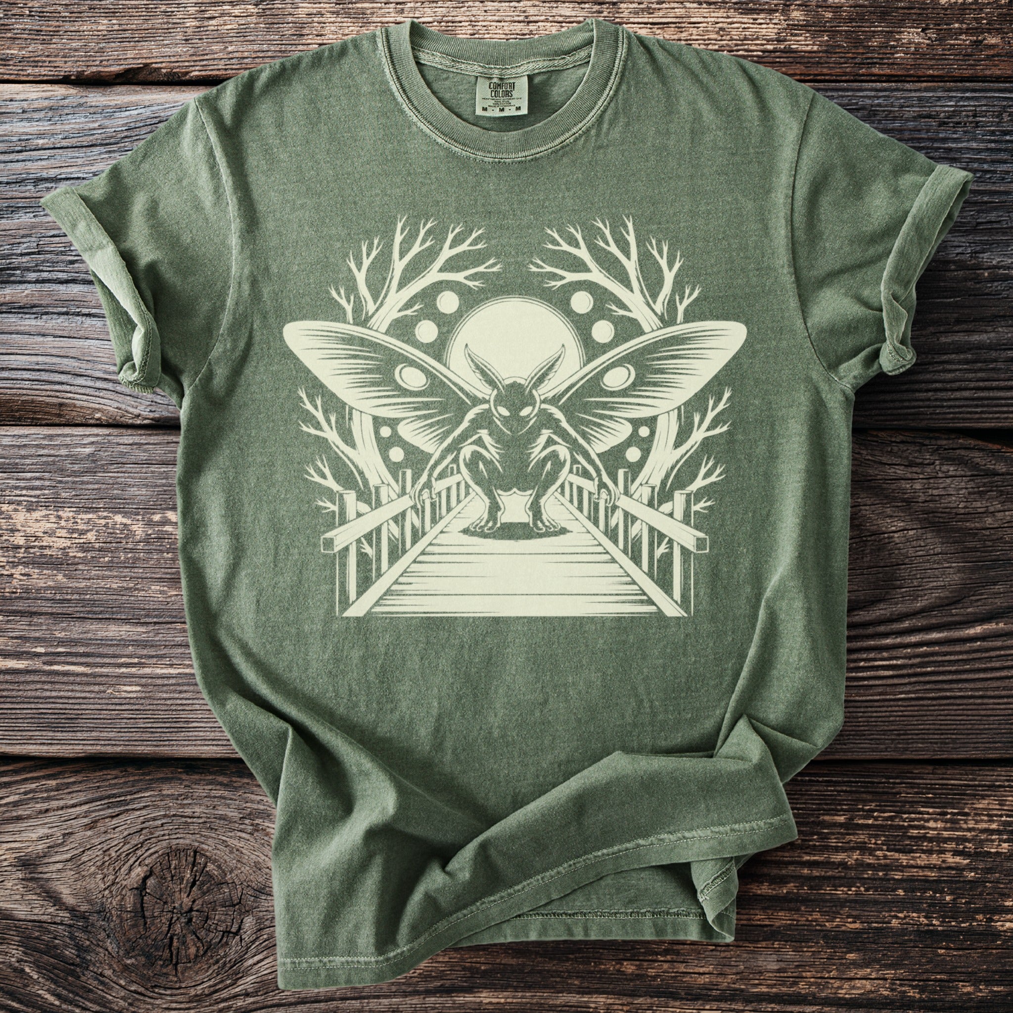 Olive green t-shirt with moth-like creature on a bridge graphic.