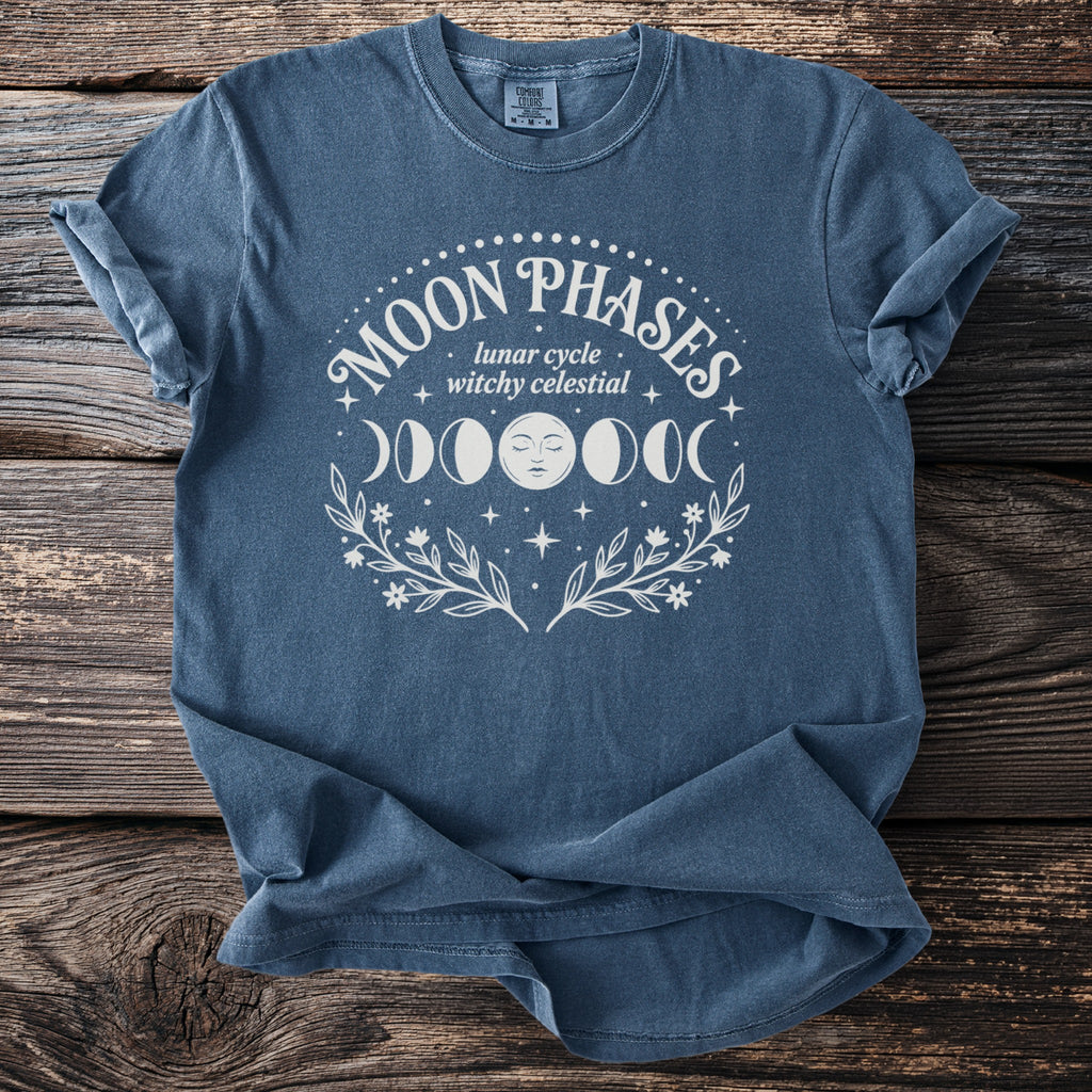Blue t-shirt with white "Moon Phases lunar cycle witchy celestial" design.