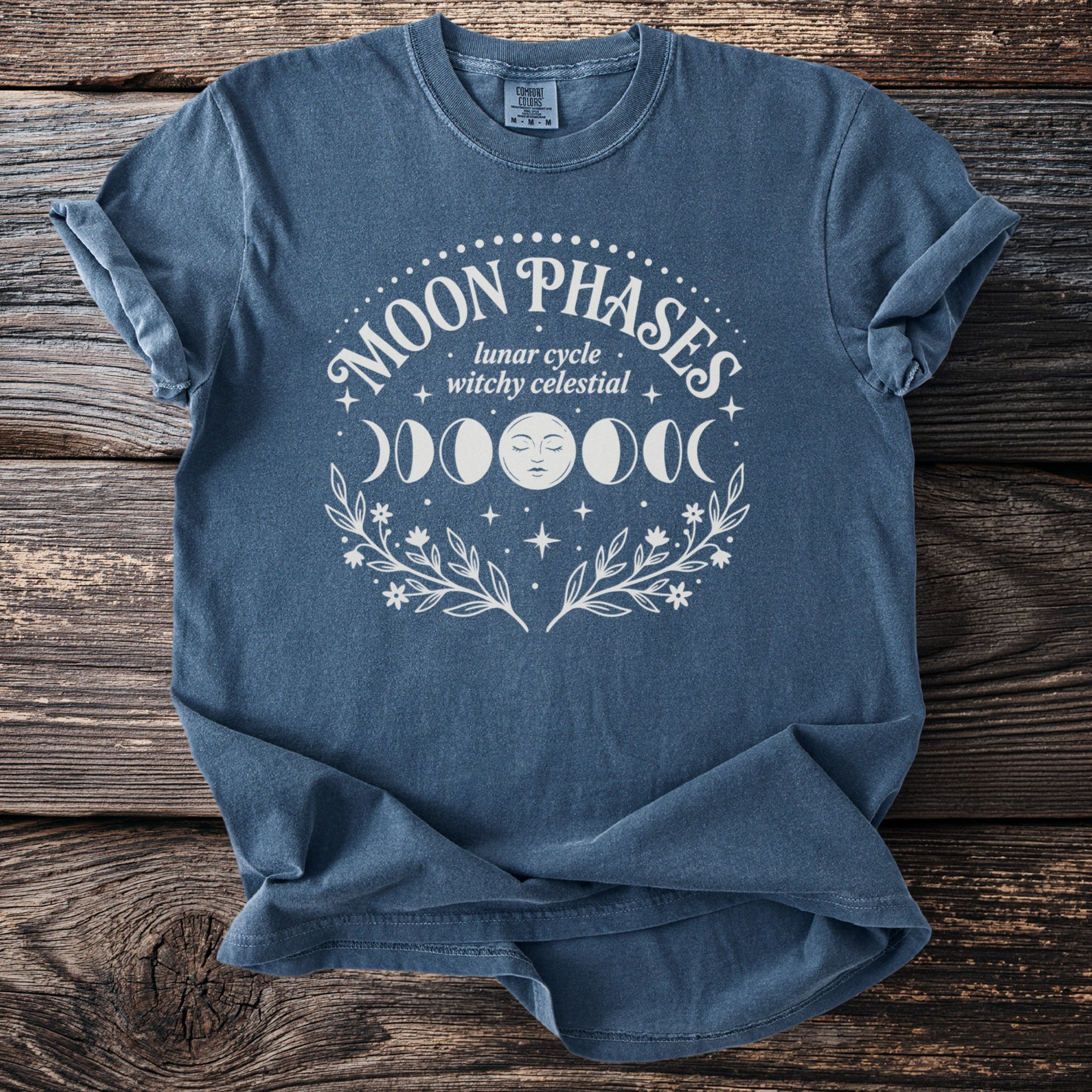 Blue t-shirt with white "Moon Phases lunar cycle witchy celestial" design.
