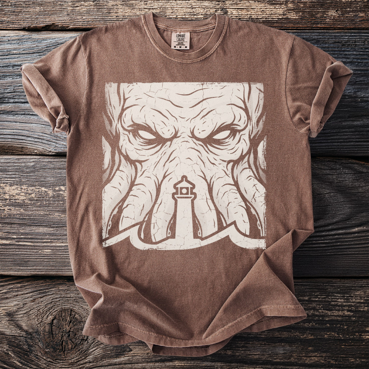 Brown t-shirt with a distressed cream graphic of a kraken's face and a lighthouse.