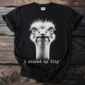 Black t-shirt with white graphic of an ostrich's face and text "i missed my flig'".