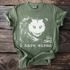 Green t-shirt with a white graphic of an opossum face and text "i have worms".
