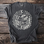 Dark grey t-shirt with white ink print of stacked books, key, moth, candle, moon and stars.