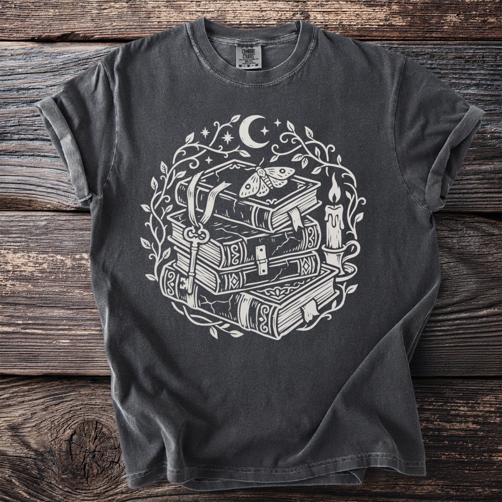 Dark grey t-shirt with white ink print of stacked books, key, moth, candle, moon and stars.