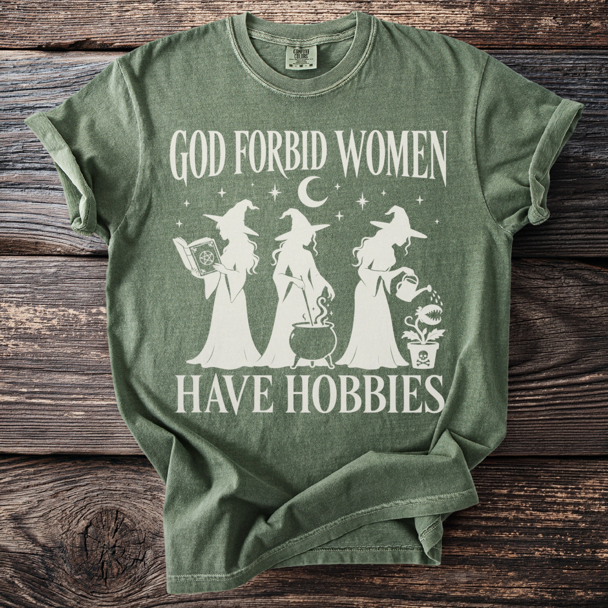 Green t-shirt with white text and witch graphic reading "God forbid women have hobbies".