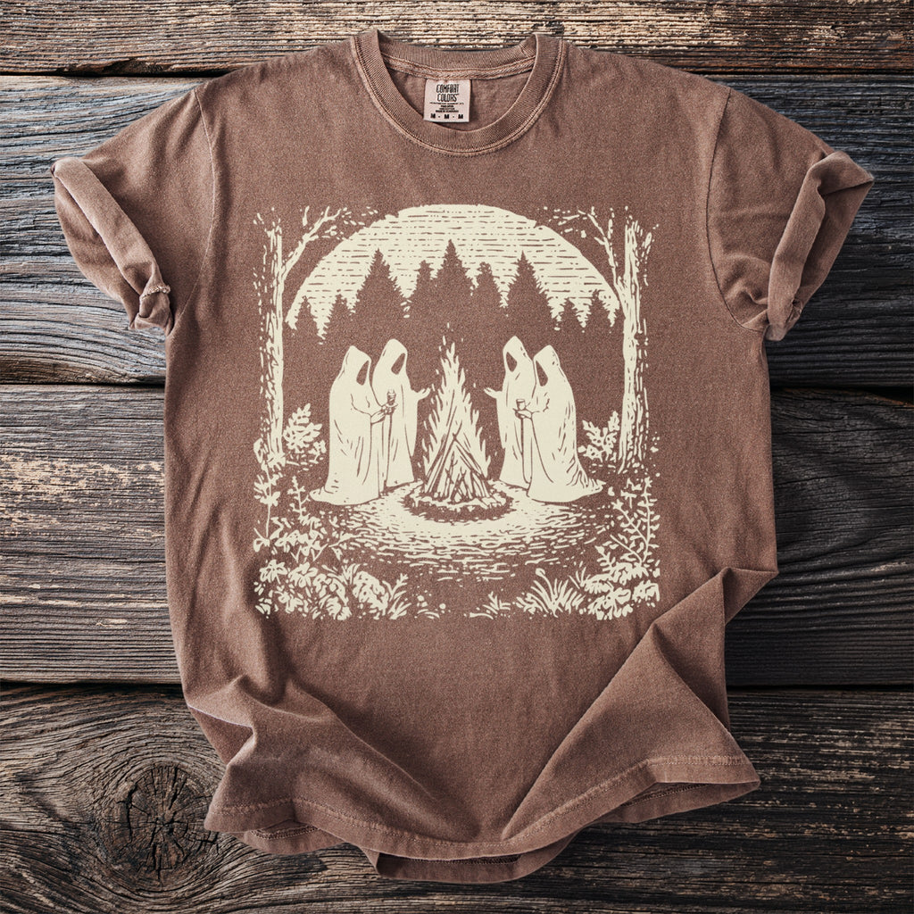 Brown t-shirt with a graphic of four cloaked figures around a campfire in a forest.