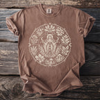 Brown t-shirt with a circular graphic featuring a woman, plants, mushrooms, candles, and moons.