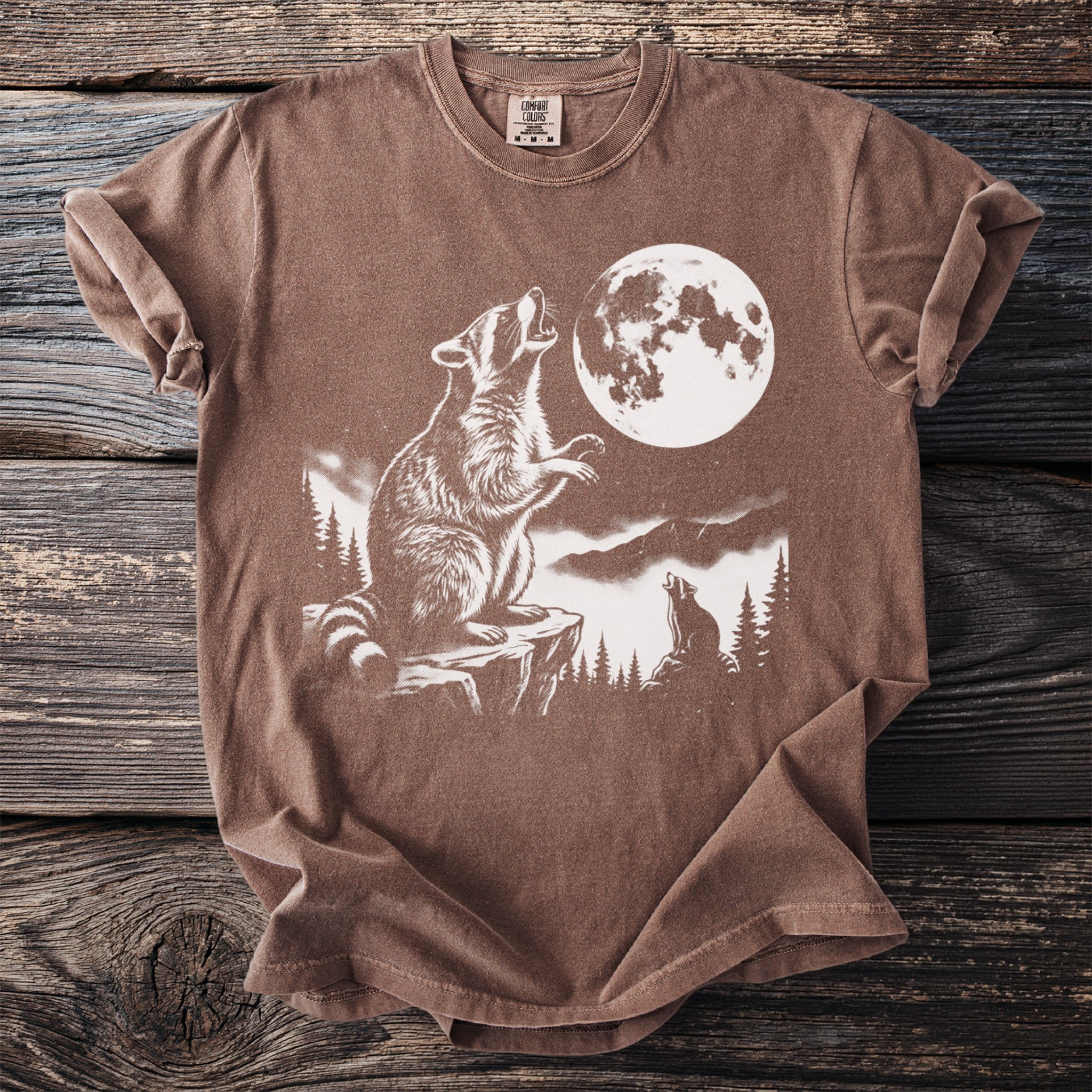 Brown t-shirt with graphic of raccoons howling at a full moon.